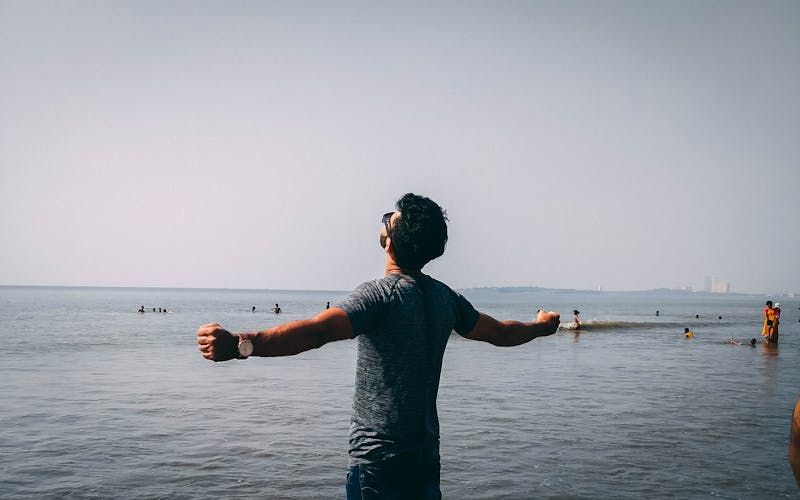 Young man standing on beach with arms wide open freeing himself from stress and anxiety