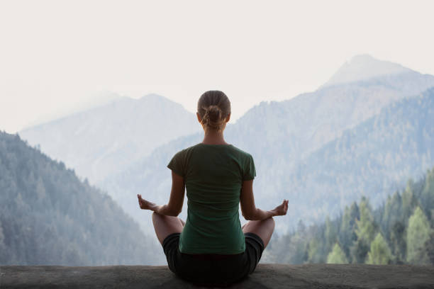 A young woman practicing transcendental meditation in the mountains in the morning, sitting cross-legged with eyes closed, surrounded by natural beauty.