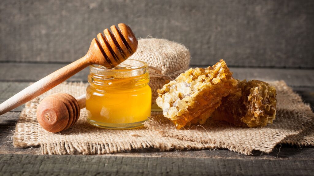 A jar of honey and various natural sources of sugar, prompting the question “how much sugar per day” when considering their consumption.