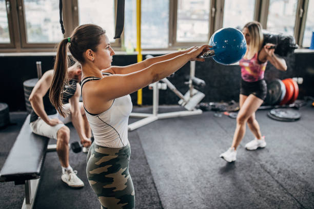 People in gym, man and two women training with weights in gym.