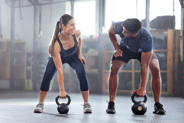 Focused man and woman lock eyes during their kettlebell workout session, intensifying their fitness commitment and connection.