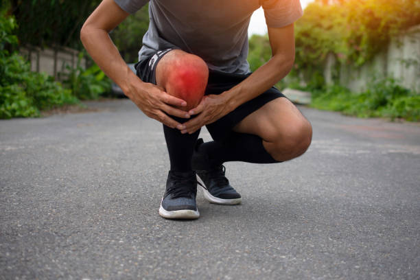 Young man bending on both knees, feeling his right knee due to pain, illustrating symptoms of arthritis in knee.