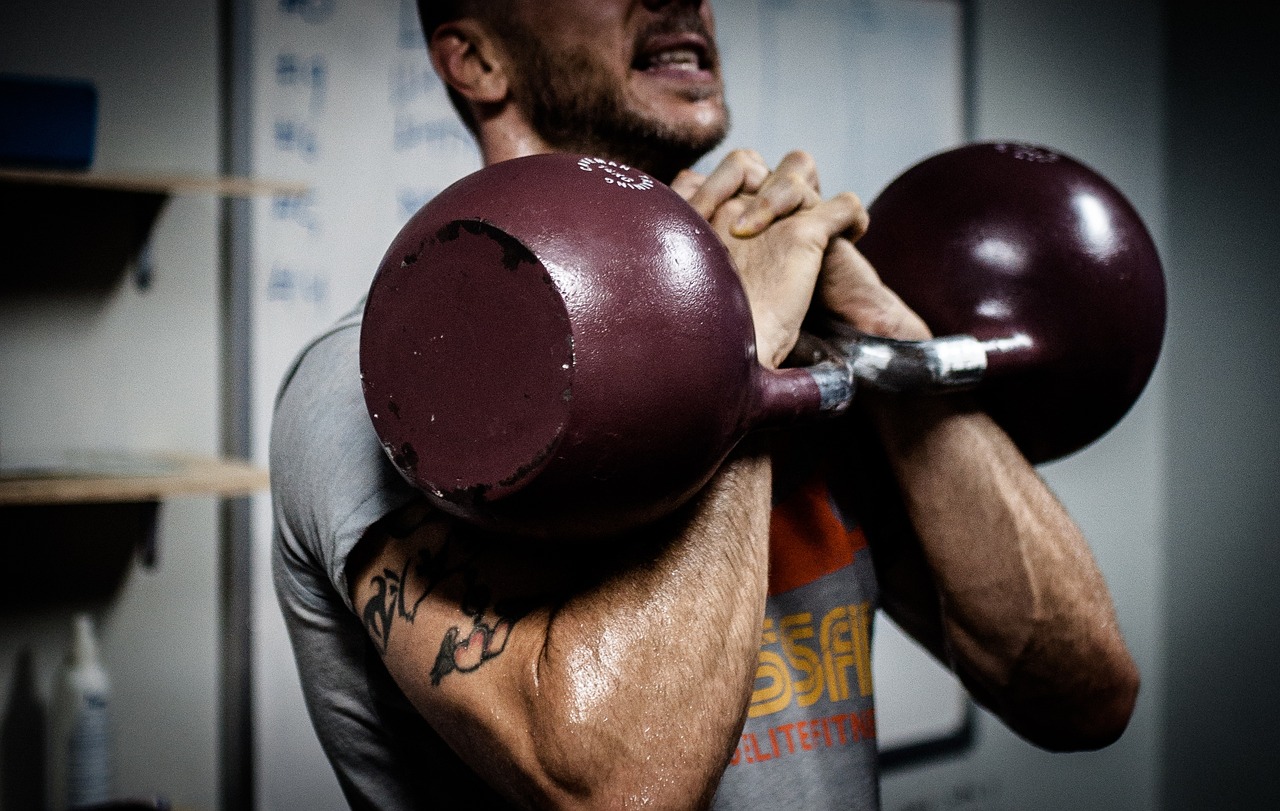 A young man performing a high intensity kettlebell workout, lifting kettlebells in both hands.