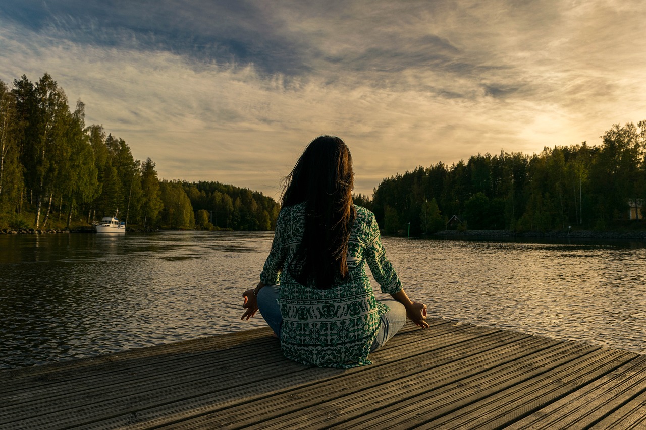 A woman practicing transcendental meditation by the lake in the afternoon