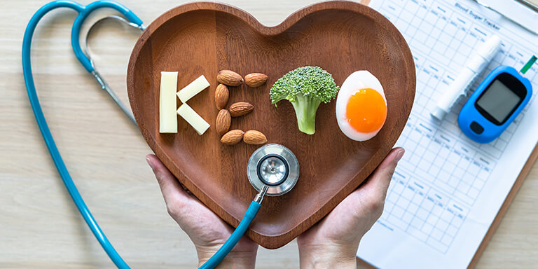 A healthcare provider holding a heart-shaped plate with ketogenic ingredients spelling out ‘keto’ and a stethoscope on the side, emphasizing the benefits of a keto diabetic diet.