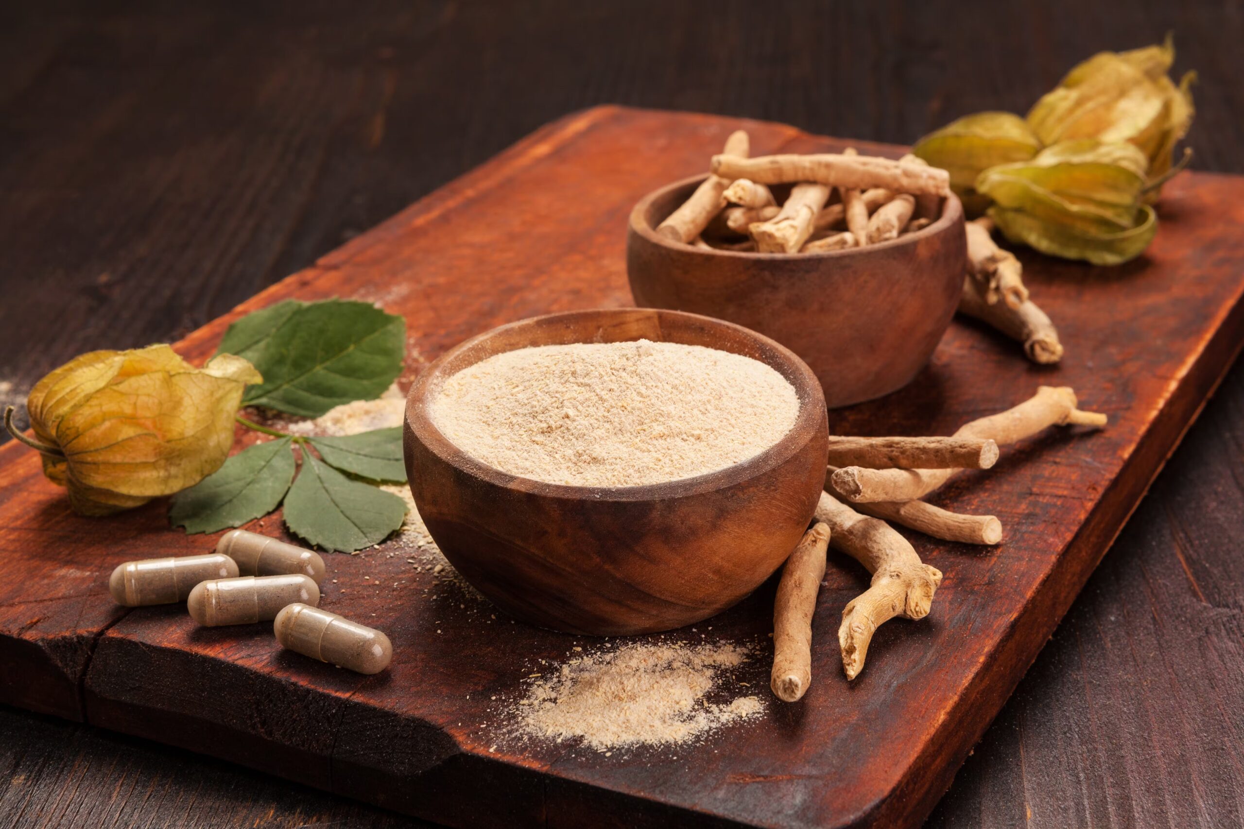 Fresh ashwagandha plant with green leaves placed next to a bowl of crushed ashwagandha root powder on a wooden surface. Natural adaptogenic herb for stress relief, anxiety reduction, and immune support.