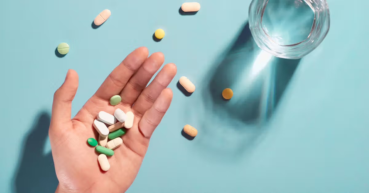 Various types of magnesium capsules and tablets held in hand, with an empty glass cup in the background—highlighting magnesium supplement options for health benefits.