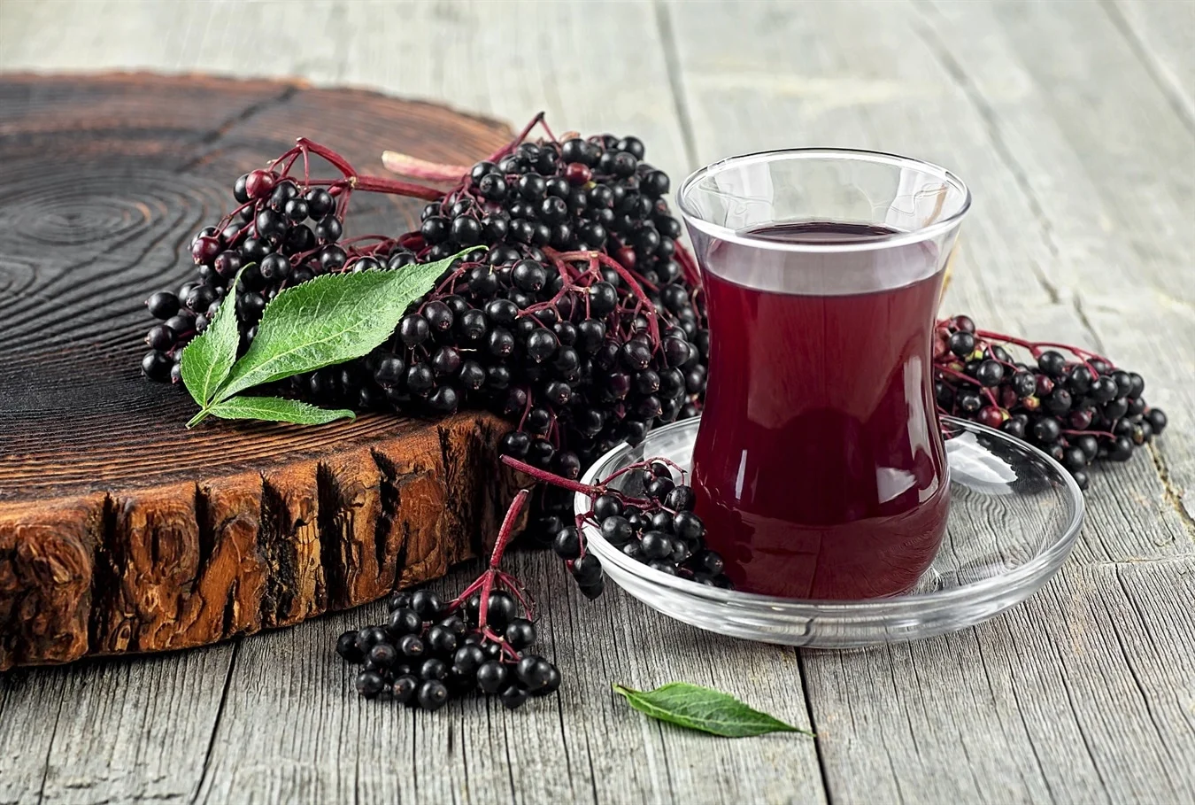 A glass cup filled with elderberry syrup, with fresh elderberries beside it. A natural immune booster rich in antioxidants for cold and flu support.