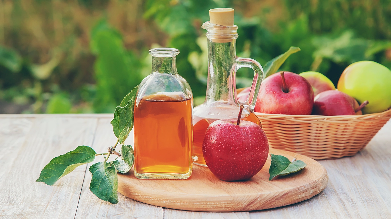 A glass bottle of apple cider vinegar with fresh apples beside it, highlighting its natural ingredients and health benefits for digestion and metabolism.